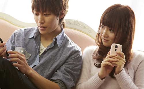 スマートフォンをいじりながら会話するカップル