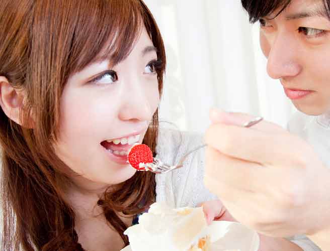 ショートケーキのイチゴを彼女に食べさせようとしてる男性