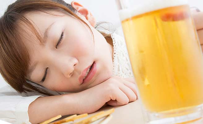 ビールを片手に机に顔をつけて目を閉じる女性