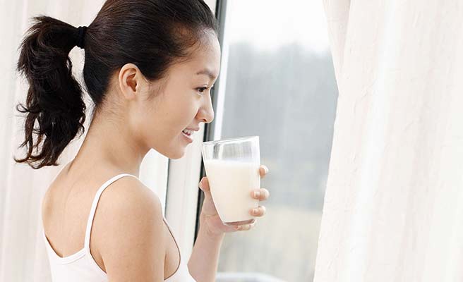 窓から外を見ながらミルクを飲む女性