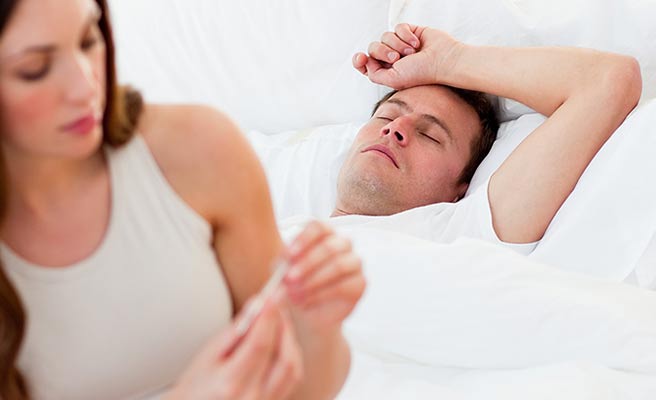 ベッドに寝る夫の熱を計る妻