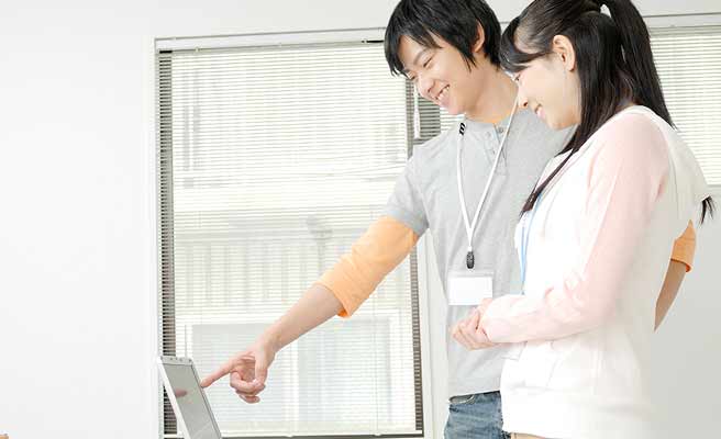 パソコンを指さす同僚男性の傍に立つ女性