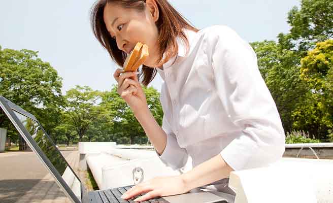 公園のベンチで昼食をとりながら仕事する女性