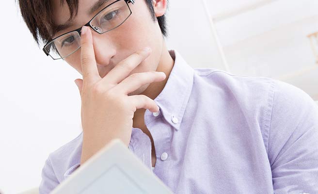 眼鏡を押さえながらノートを読むインテリ男性