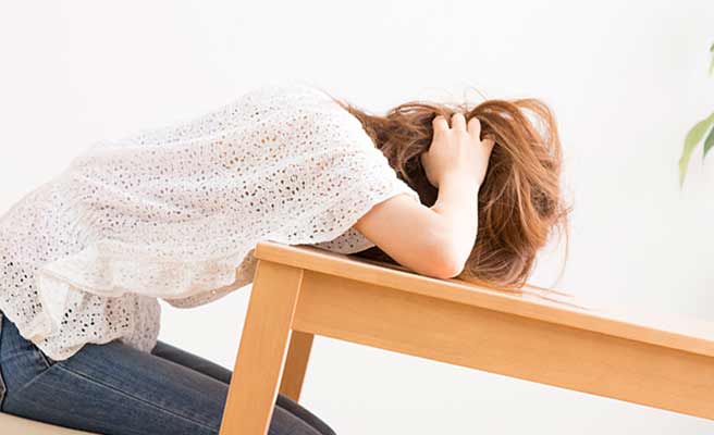 机に頭をつけて悩む女性