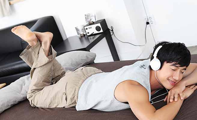 部屋で横になってヘッドホンで音楽を聴く男性