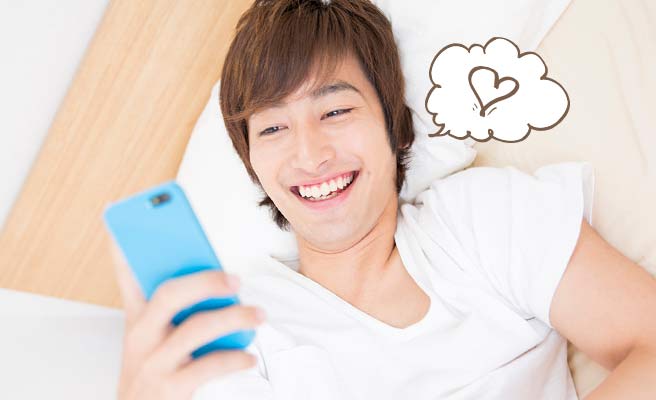 ベッドに横になったままスマホを見て笑う男性