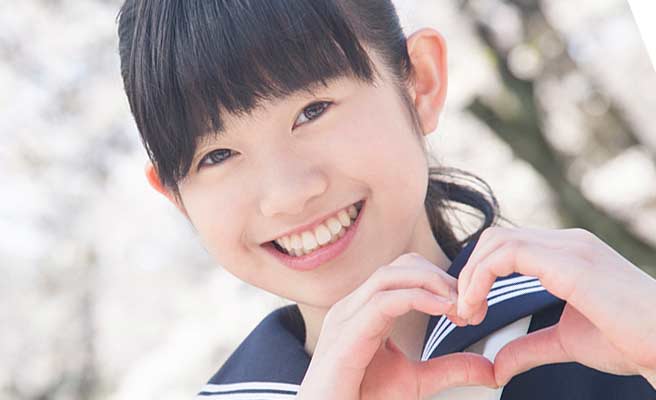 笑顔でハートマークを手で作る女子中学生