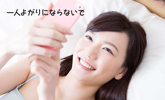 ベッドに横になりながらスマホを見つめる女性